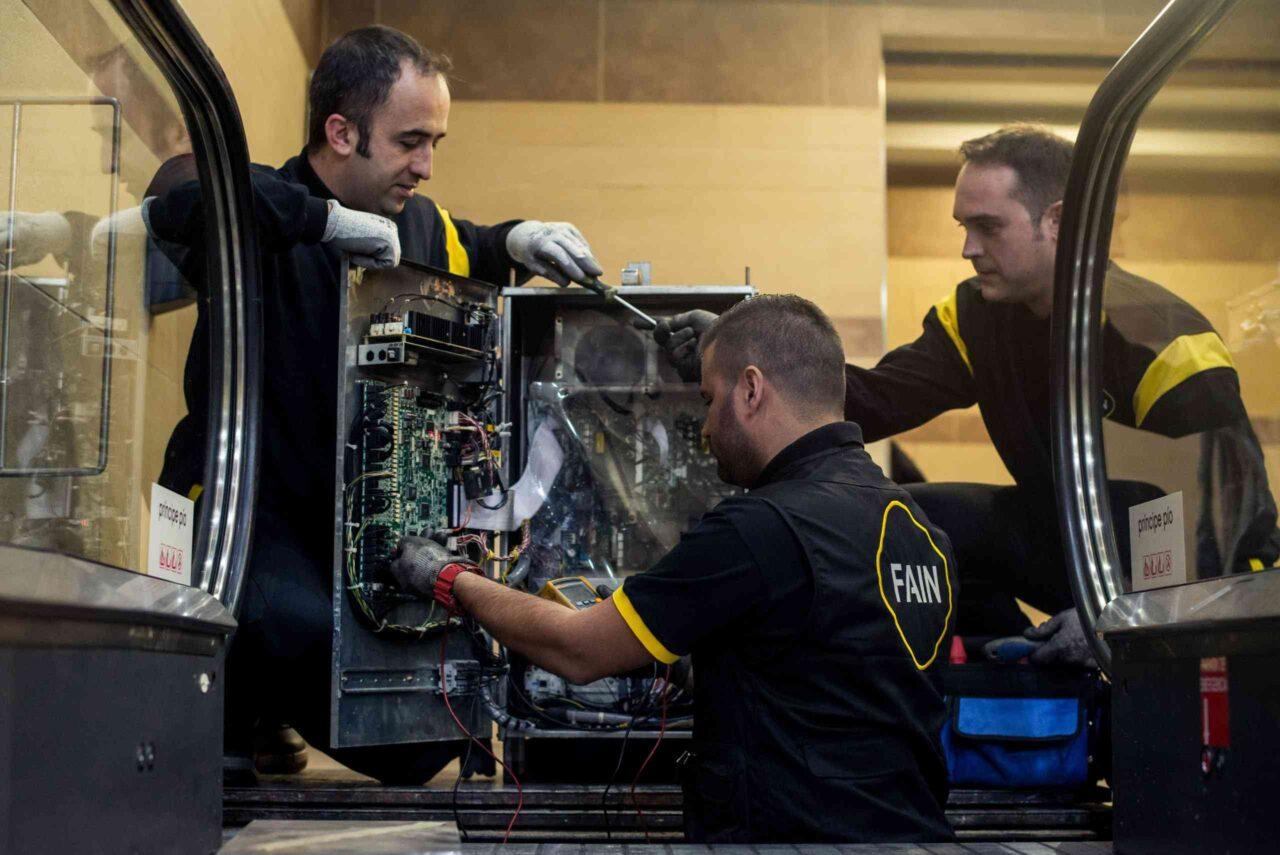 Tres técnicos FAIN revisando estado de escalera mecánica