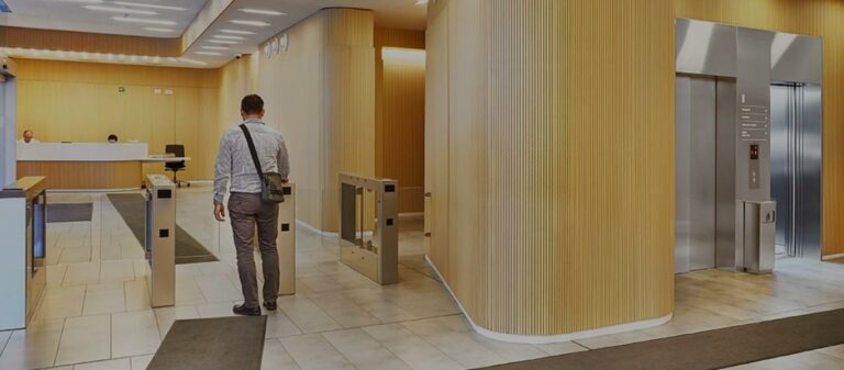 Persona acercándose a un torniquete de acceso en un edificio moderno con diseño en madera y baldosas.